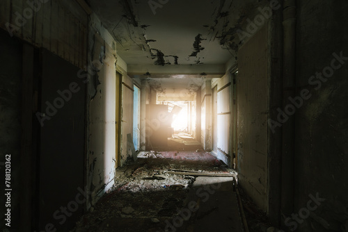 Decayed corridor in derelict building with sunlight streaming through the end.