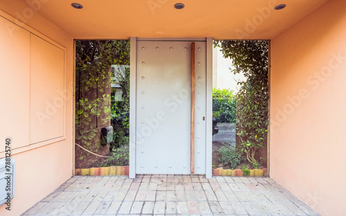 A modern design house entrance with a metal pale gray door and a garden behind the glass openings. Travel to Athens, Greece.