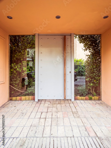A modern design house entrance with a metal pale gray door and a garden behind the glass openings. Travel to Athens, Greece.