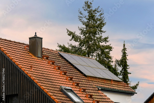 Photovoltaikanlage auf rotem Hausdach vor Bäumen und Abendhimmel