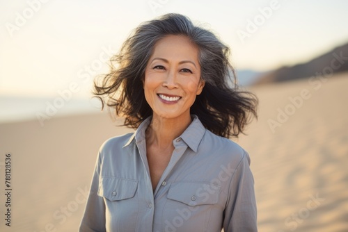 Portrait of a jovial asian woman in her 60s sporting a versatile denim shirt in front of serene dune landscape background
