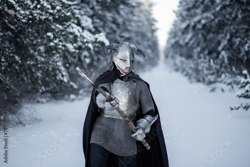 Portrait of a medieval fantasy warrior in a horned helmet, steel cuirass, chain mail with a two-handed ax in his hands, standing in a fighting position against the backdrop of a winter forest.
