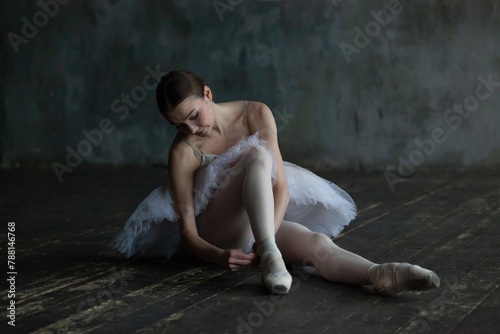 Ballerina sits on the floor and adjusts her pointe shoes.