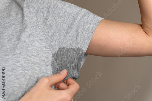 Close-up of a young woman shows a wet armpit on a gray T-shirt. Concept of health, sports