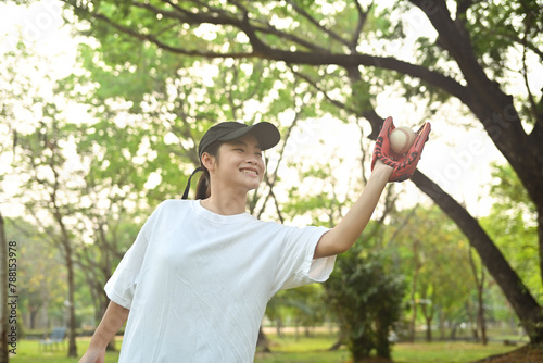 Shot of teenage Asian girl wearing leather glove playing baseball in the park photo