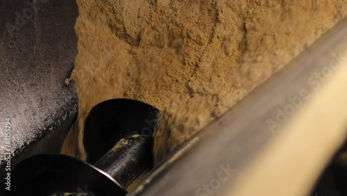 Close up of large part of heavy machinery mechanism working at production of cattle feed. Screw rotating inside funnel filled with crushed wheat and corn during sifting process.
