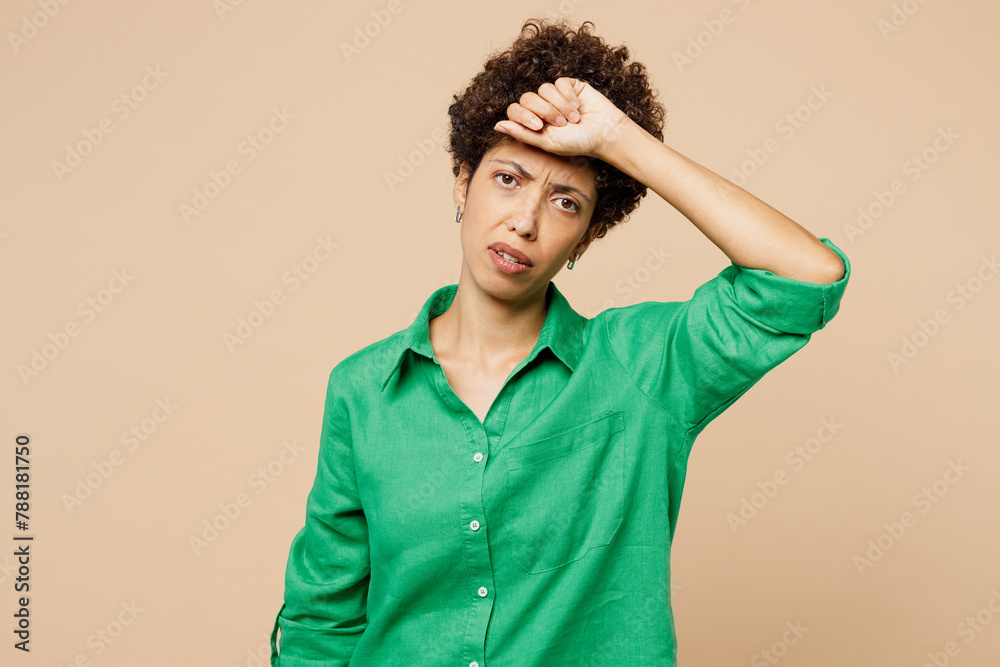 Young sick ill sad woman of African American ethnicity wears green shirt casual clothes put hand on forehead suffer from headache isolated on plain pastel beige background studio. Lifestyle concept. Young sick ill sad woman of African American ethnicity wears green shirt casual clothes put hand on forehead suffer from headache isolated on plain pastel beige background studio. Lifestyle concept.