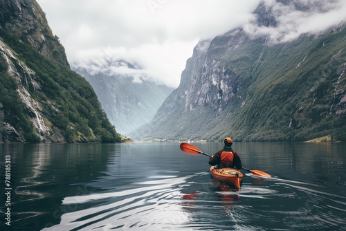 A man in a life jacket paddles a kayak along a beautiful fjord surrounded by mountains, rear view