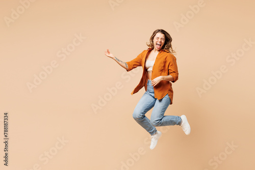 Full body expressive overjoyed cool singer young woman she wear orange shirt casual clothes jump high play air guitar isolated on plain pastel light beige background studio portrait Lifestyle concept