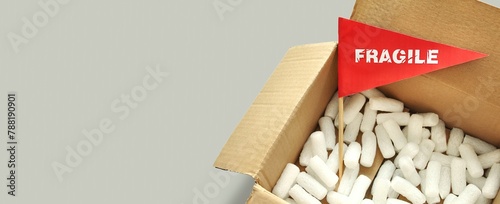 Opened cardboard packaging box with white polystyrene packing chips inside. Tiny red paper flag with the warning 'Fragile' as a label, sticker. The concept of packing and shipping fragile items photo
