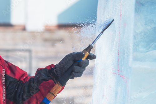 A sculptor processes a large ice cube with a sharp hand tool. Ice dust and ice fragments in the air. Ice sculpture festival.