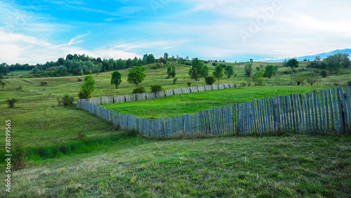 A wooden fence built on a hill. The meadows on the hill are used for farming or for orchards. Rural landscape aof traditional farming in Eastern Europe.  photo