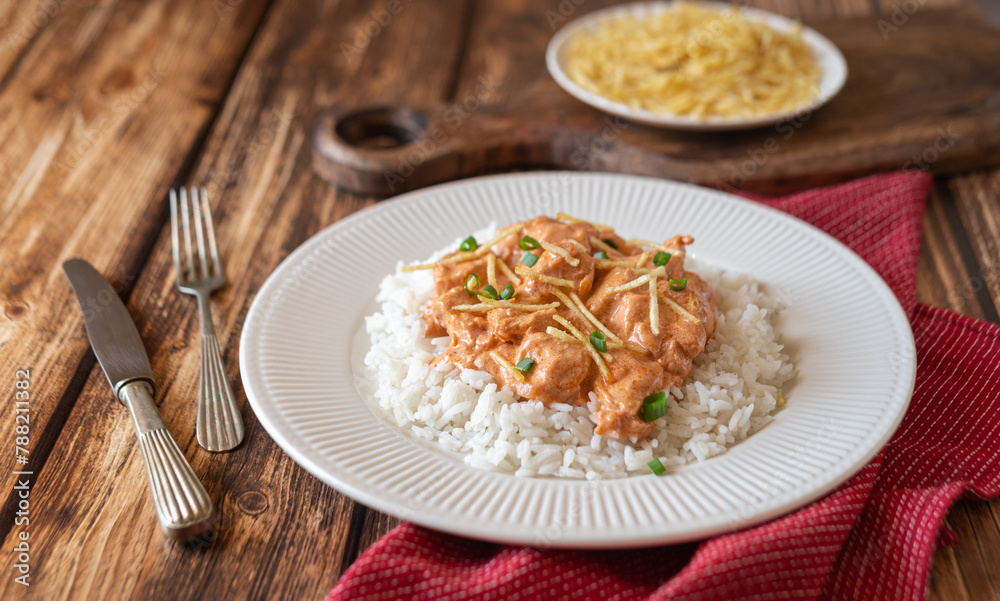 Brazilian style Chicken strogonoff with rice and potato straw on wooden table.