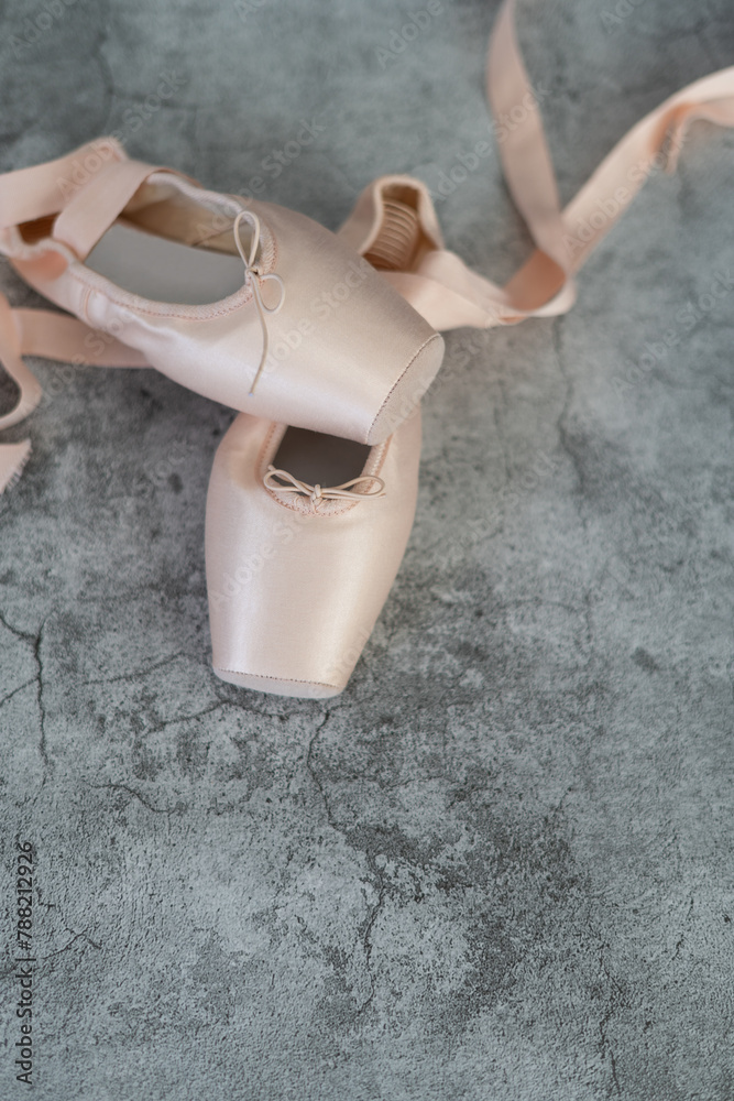 A pair of pink ballet slippers isolated on a gray surface, in vertical image. - obrazy, fototapety, plakaty 