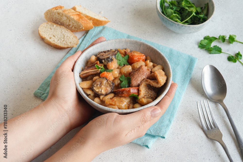 Female hands holding a bowl with Portuguese tripas - Tripe stew on the white table. Traditional gastronomy concept. - obrazy, fototapety, plakaty 