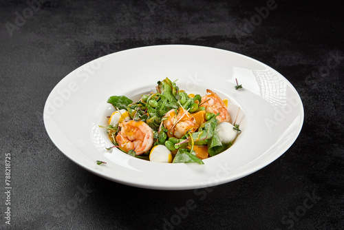 Healthy food - shrimp salad with mango, lettuce and mozzarella cheese on black background. Fresh salad with prawns and mango sauce. Seafood salad with cheese and mango on dark background.