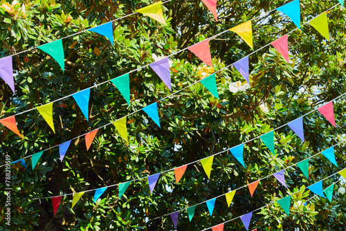 Multicolored flags hangs in front of lush green foliage for summer festival in June San Juan