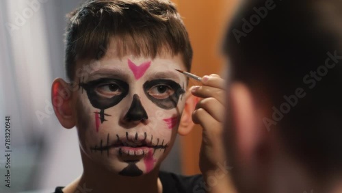 A boy of 9 years old, looking in the mirror, paints his face in a mystical image with makeup for the holiday of Halloween or the Day of the Dead. children and Halowin celebration photo