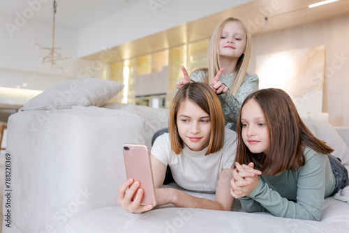 Three girls are laying on couch, one of them holding a cell phone