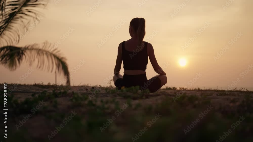 Woman practices yoga on ocean at sunset. Silhouette sporty yoga girl doing yoga pose asana exercise meditation at sunset on beach in nature close up. Health, professional yoga, harmony concept. Woman practices yoga on ocean at sunset. Silhouette sporty yoga girl doing yoga pose asana exercise meditation at sunset on beach in nature close up. Health, professional yoga, harmony concept.