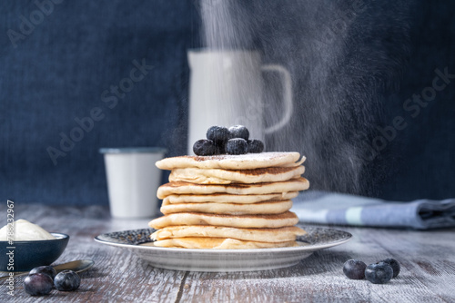Straigh on view of a stack of pancakes with dusting of icing sugar and blueberries