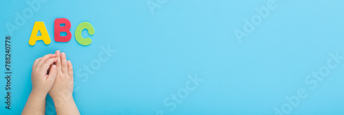 Baby boy hands and colorful abc letters on light blue table background. Pastel color. Time to learning. Closeup. Point of view shot. Wide banner. Empty place for text. Top down view.
