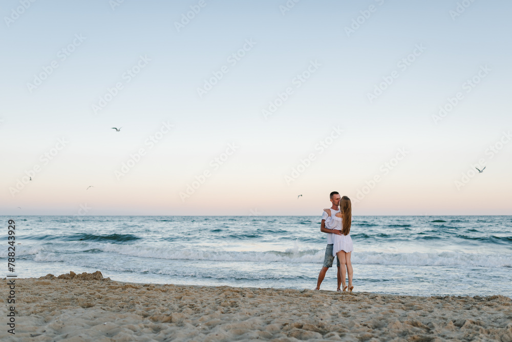 Man embraces woman walking on sand sea. Couple in love hugging and ...