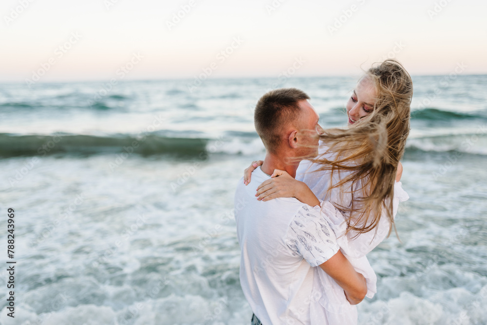 Happy people spend time together. Couple in love hugging on seashore in sea. Male hugs female standing on water with big waves ocean and enjoying summer day. Man embraces woman walk on beach sand sea. Happy people spend time together. Couple in love hugging on seashore in sea. Male hugs female standing on water with big waves ocean and enjoying summer day. Man embraces woman walk on beach sand sea.