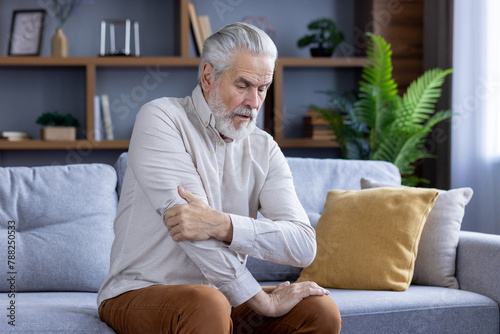 Senior man with shoulder pain sitting on sofa at home