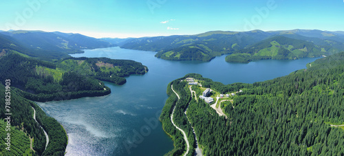 Aerial drone panorama above Vidra lake in a sunny day. The lake is surrounded by mountain crests covered with wild coniferous forests. A tourist resort lies at the lake s side. Carpathia  Romania.