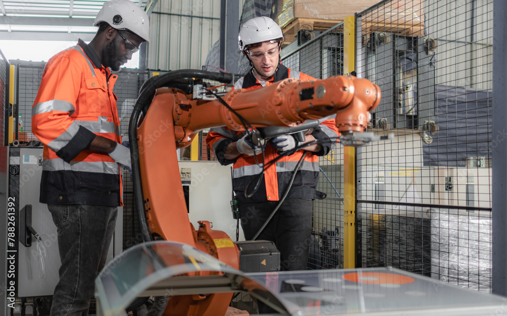Diverse group of engineer in safety uniform maintenance and examining robot arm machine in modern engineering factory. Multiracial technician and caucasian inspector working together in Industry