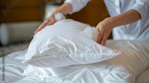 Housekeeping hand fluffing a pillow, detailed shot, soft textures, guest comfort, room preparation photo