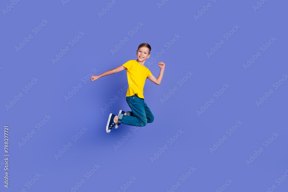 Full length photo of cheerful optimistic active boy wear stylish yellow clothes fly air yeah success isolated on violet color background Full length photo of cheerful optimistic active boy wear stylish yellow clothes fly air yeah success isolated on violet color background