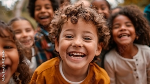 A group of children are smiling and laughing together, the boy in the center is wearing a yellow shirt