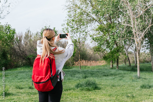 Fotografija Hiker with his back turned to take out his phone to take photos during a field t