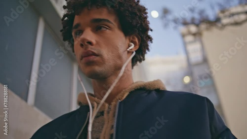 Mixedrace guy listening song in earphones strolling city closeup. Curly teenager photo