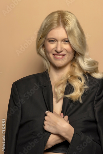 Beauty portrait of fashion young model with long blond hair and funny smile on beige background