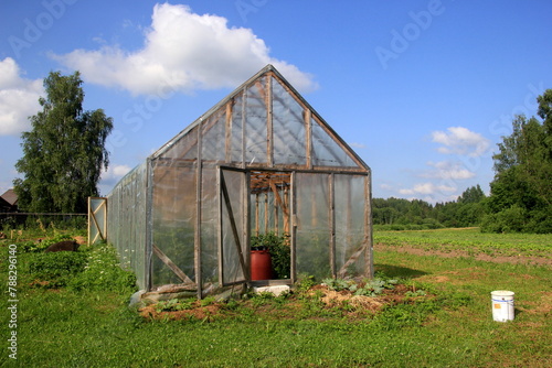 A large red barrel of water stands in the door of the wooden greenhouse. Water barrel for watering plants © Art Johnson