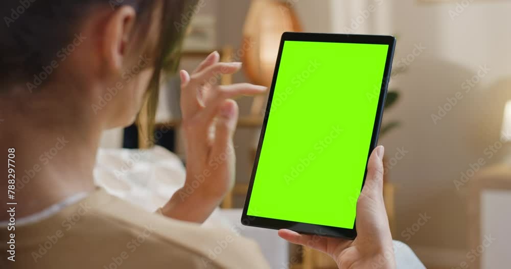 Close up view of woman working with tablet at well designed home. Female scrolling mock up screen. Woman using device with chroma key screen. Female looking at green template display.