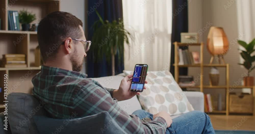 African american man sitting at couch. Man relaxing at well desighend room. Male sitting at sofa and holding smartphone. Man managing cryptocurrency. Back view of man working at home. African american man sitting at couch. Man relaxing at well desighend room. Male sitting at sofa and holding smartphone. Man managing cryptocurrency. Back view of man working at home.