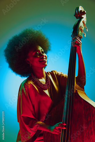 Portrait of overjoyed African-American woman, double-bass player performing in neon light against gradient background. Concept of art, music, hobby, classical music and modern lifestyle. Ad