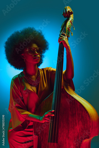 Photography Vintage style African-American woman, jazz performer with glasses posing with double bass in neon light against gradient background