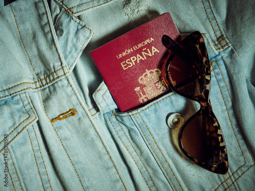 A Spanish passport in a denim jacket pocket and sunglasses