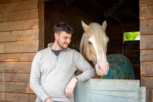 Man with a horse, Image shows a 28 year old bearded male posing with a palomino section D Welsh cob pony, stallion in it's stable on a small farm in Surrey