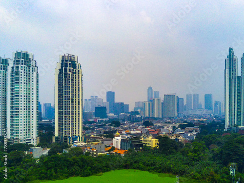 A cityscape view in Kuningan, Jakarta with tall buildings and lush trees in the foreground.