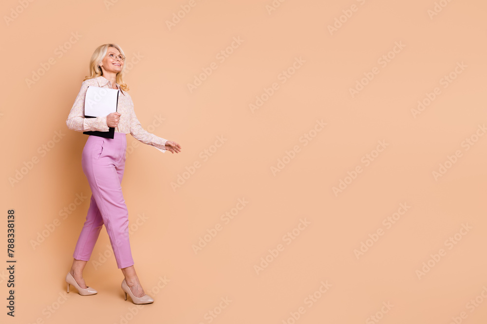 Full body photo of retired female hold paperholder documents walk empty space wear trendy formalwear isolated on beige color background Full body photo of retired female hold paperholder documents walk empty space wear trendy formalwear isolated on beige color background