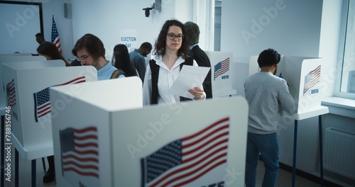 Woman in glasses comes to vote in booth in polling station office. National Elections Day in United States. Political races of US presidential candidates. Civic duty concept. Slow motion. Dolly shot. photo