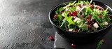 A black bowl on a chalkboard background filled with a refreshing spring salad comprising rucola, feta cheese, red onion, and pomegranate seeds, with available space for text.