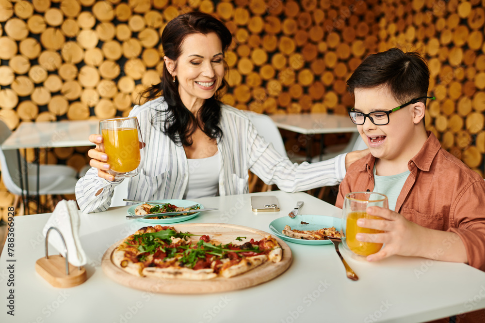 happy mother eating pizza and drinking juice with her inclusive cute son with Down syndrome happy mother eating pizza and drinking juice with her inclusive cute son with Down syndrome