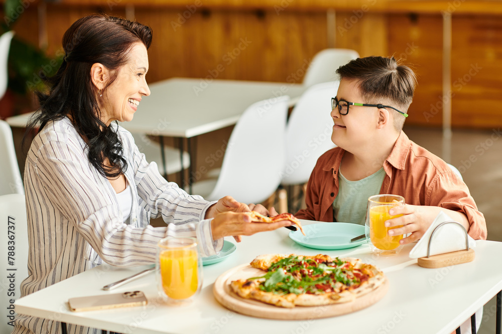 attractive mother eating pizza and drinking juice with her inclusive cute son with Down syndrome